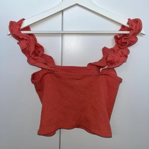 Ribbat linne - Ett ribbat linne med snurrade axelband. Färgen kan beskrivas som korall eller en blandning av rosa/orange. Lappen i ryggen är bortklippt. Haft mycket glädje av linnet men det syns inte på dess skick.