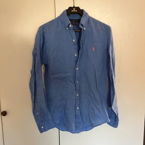 Blå linneskjorta från Ralph Lauren - Säljer en blå slim fit skjorta från Ralph Lauren i svalt linne. Passform slimfit och är inye super mycket använd. Vid fråga är det vara att skrivan! 