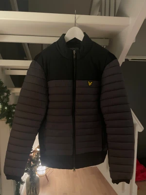 Svart och grå pufferjacka från Lyle & Scott - Säljer en stilren pufferjacka från Lyle & Scott i svart och mörkgrått. Jackan är i storlek S å är köpt i butik nypris 1500, den är i väldigt bra skick.
