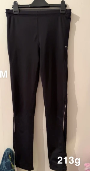 Svarta träningsleggings med dragkedja - Svarta träningsleggings med smal passform och dragkedjor vid bensluten. Perfekta för löpning eller gym, tillverkade i ett stretchigt material som andas. Diskret logga på ena benet och elastisk midja för extra komfort.🌸Fint använt skick. Storlek m