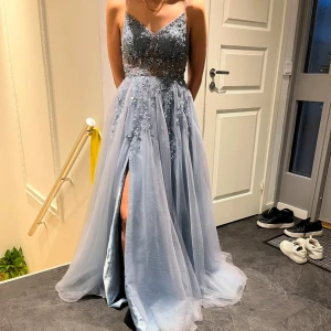 Ljusblå långklänning med paljetter - Elegant ljusblå långklänning med glittrande paljetter och en djup slits. Klänningen har en v-ringad design och tunna axelband, vilket ger en stilren look. Perfekt för speciella tillfällen. Perfekt till bal.