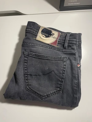 Jacob Cohën jeans - Säljer ett par snygga Jacob Cohen jeans i en klockren mörk grå färg. Jeansen har storleken 33 och är modellen MOD. Dem är i ett mycket fint skick. Det ända jag anser är lite konstigt är byxknapoen låter lite konstigt men det påverkar inte hur byxorna sitter. Mått: Midja, 42 Cm. Lår, 25 Cm. Ytterlängd, 90 cm, Innerlängd 60 Cm. Hör av dig om du undrar något 