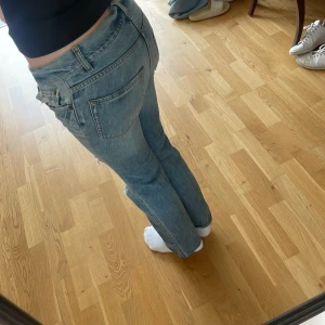 Ljusblå lågmijade bootcut jeans - Säljer ett par ljusblå jeans med bootcut passform och snygga slitningar och hål på benen. Jeansen har klassisk femficksdesign, låg midja och är tillverkade i mjukt denim. Perfekta för dig som gillar en avslappnad och trendig look.