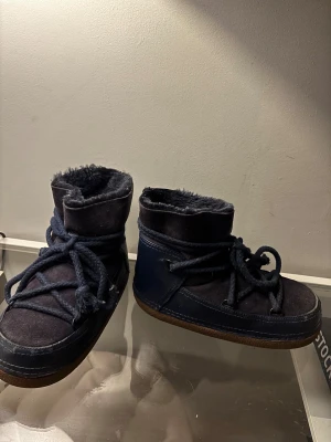  Inuikii classic boots mörkblå - Moon boots från Inuikii i mörkblå färg Utsidan är i mocka och skinn, insidan är fodrad med mjuk päls för extra värme. Använda förra vintern men inga större skråmor och väldigt fina Storlek 38 Nypris 3800kr