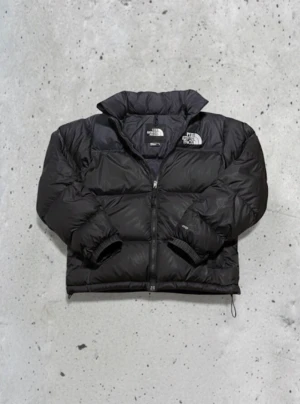  The North Face 700 vinter jacka S - Säljer en svart pufferjacka från The North Face med klassisk logga på bröstet och ryggen. Jackan har hög krage, långa ärmar och dragkedja framtill. Fylld med dun och har en loose passform, perfekt för kalla dagar. Snygg och enkel design som funkar till allt.