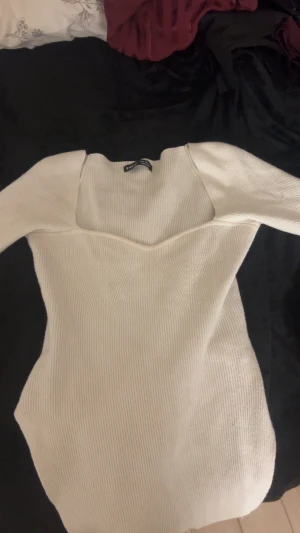 Vit ribbad klänning från SHEIN - Säljer en vit ribbad klänning från SHEIN med lång ärm och snygg v-ringad urringning. Klänningen är figurnära och har en stretchig, stickad känsla som framhäver siluetten. Perfekt för dig som gillar minimalistisk och clean stil.