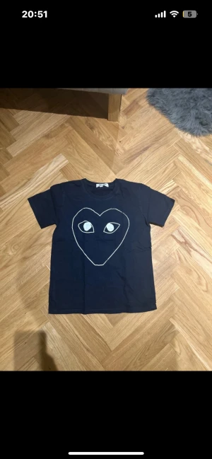 Mörkblå Comme des Garçons Play t-shirt - Mörkblå t-shirt från Comme des Garçons Play med stort hjärta i vitt på bröstet. Den är i bra skick (9/10. Det är en storlek M men den sitter som en S. Det är bara höra av er om ni har några frågor eller funderingar. Mvh Olof