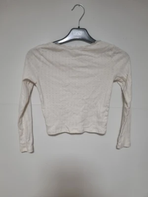 Vit långärmad blus med rosett H&M - Söt vit långärmad blus från H&M med små prickar i tyget, spetskant vid halsen och en liten rosett framtill. Croppad passform som ger en trendig look. Perfekt att styla med jeans eller kjol för en chill vibe.