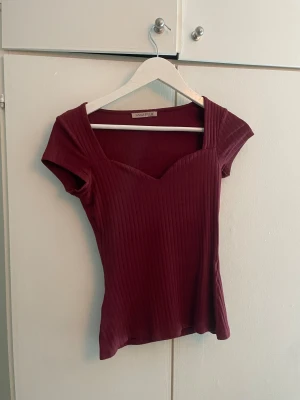 Vinröd ribbad topp från Anna Field - Säljer en vinröd ribbad topp från Anna Field med snygg v-ringad sweetheart-urringning och korta ärmar. Toppen har en slim passform och är tillverkad i mjuk bomull som sitter skönt mot kroppen. Perfekt för dig som gillar stilrena detaljer och en modern look.