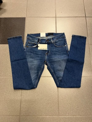 Blå slimmade jeans Tiger of Sweden W29 L32 - Snygga blå jeans från Tiger of Sweden med smal passform och smala ben. Klassisk femficksmodell med läderpatch bak och detaljer i gult. Tillverkade i mjuk bomullsdenim med stretch för extra komfort.