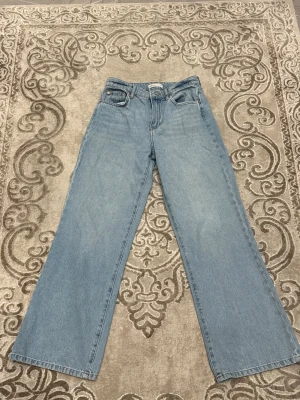 Perfekt ljusblå wide jeans från Gina Tricot  - Snygga ljusblå jeans, modell Perfect Jeans från Gina Tricot. De har klassisk femficksdesign, hög midja och breda ben för en chill och trendig look. Materialet är jeans och passformen är loose med raka, vida ben. Perfekt för dig som gillar retrovibbar och bekväma outfits.