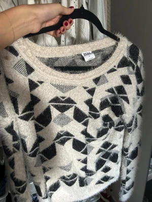Mönstrad fluffig tröja Vero Moda M - Fluffig och mjuk tröja från Vero Moda i storlek M. Tröjan är beige med svart geometriskt mönster, har rund hals och långa ärmar. Materialet är stickat och ger en mysig känsla (sticks inte) perfekt för kyliga dagar. Snygg att matcha med jeans eller kjol💕💕