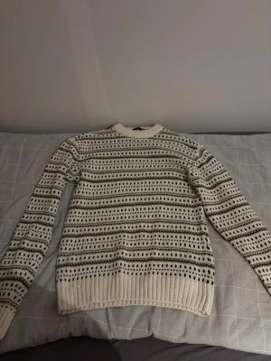 Vit och svart stickad tröja med mönster - Säljer en vit stickad tröja med svarta och gråa ränder och ett snyggt mönster över hela tröjan. Tröjan har rund halsringning, långa ärmar och ribbade muddar 9/10 skick storlek S, har använd 1 gång vid fler frågor bara skicka Mvh Emil🙂