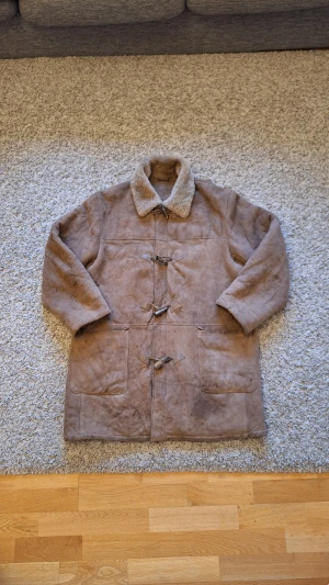 Brun duffel jacka från Canterbury Leather International  - Snygg varm brun duffel jacka från Canterbury Leather International i storlek M(passar L också). Använd fåtal gånger och skicket är jättebra. Den har dock lite slitningar men det påverkar inte jackans skick som helhet(fråga gärna för fler bilder). Jackan har två fickor och fyra knappar samt en dragkedja. Den har också plysch på insidan som kommer att hålla dig både varm och stilig nu under vintern! Skick: 8/10