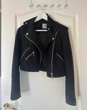 Svart croppad mochajacka med dragkedjor - Snygg svart croppad mochajacka med flera silvriga dragkedjor och detaljer. 