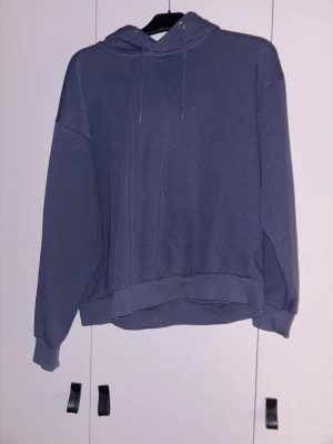 Mörkblå hoodie med huva och snörning - Säljer en enkel och stilren mörkgrå hoodie med huva och snörning. Tröjan har långärmade ärmar och ribbade muddar vid ärmslut och nederkant. Perfekt för chill dagar och passar till det mesta. Oversized passform för extra komfort.