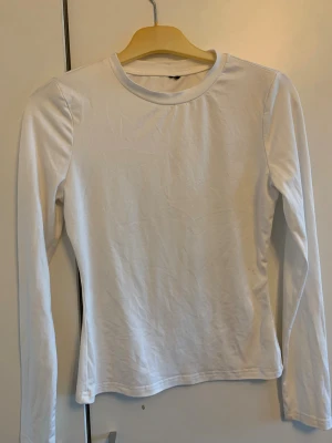 Vit långärmad topp i bomull - Säljer en enkel och stilren vit långärmad topp i mjuk bomull. Modellen har rund hals och en slim passform som sitter snyggt på kroppen. Perfekt att matcha med jeans eller kjol för en clean look.