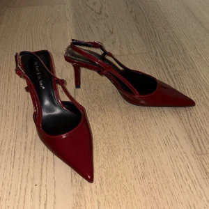 Vinröda lackade pumps med klack - Snygga vinröda pumps i lackad syntet med spetsig tå och smal klack. Skorna har öppen häl med justerbar rem och ger en riktigt trendig vibe.