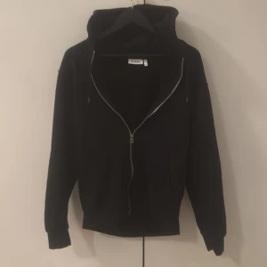 Svart hoodie med dragkedja från Weekday - Svart hoodie från Weekday i storlek XS. Klassisk modell med huva, långa ärmar och hel dragkedja framtill. Perfekt basic-plagg med ribbade muddar och mjukt material. Snygg och enkel att matcha till allt. Köpt för ca 600 mitt pris 300.