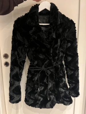 Svart pälsjacka från Vero Moda - Snygg svart pälsjacka från Vero Moda med markerad krage och knytband i midjan.  Knytbandet är avtagbart. Mycket fint skick!