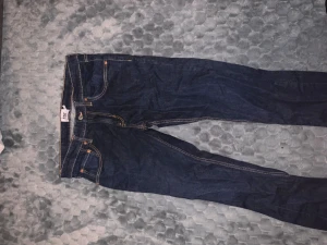 Lager 157 mörkblå jeans - Snygga mörkblå lager 157  jeans med klassisk femficksdesign och kontrastsömmar. Modellen är slim och har en rak passform som sitter tajt över benen. Perfekta för dig som gillar en stilren och modern look.