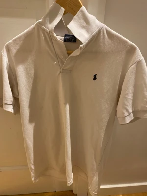 Vit pikétröja från Ralph Lauren - Snygg vit piké. Säljer för den blivit för liten. Mindre fläckar på framsidan som jag visar i bilen, men inget som syns i vanliga fall.