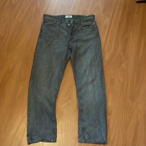 Gråa jeansbyxor från jack and jones W30 L30 - Säljer ett par gråa jeansbyxor från jack and jones i klassisk rak modell. Jeansen har fem fickor, bälteshällor och en snygg tvättad finish. Perfekta för dig som gillar en enkel och stilren look. Storlek W30 L30.