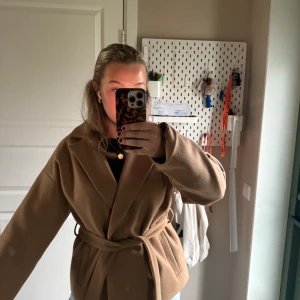 Beige kort kappa med bälte från ICHI - Säljer en snygg beige kappa från ICHI med bälte i midjan. Sparsamt använd och i fint skick. Nypris 1300kr