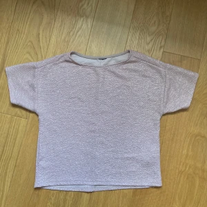 Glittrig ljusrosa topp från Gina Tricot - Säljer en glittrig ljusrosa topp från Gina Tricot i boxig modell. Toppen har korta ärmar, rund halsringning och är tillverkad i ett stretchigt polyestertyg med skimrande effekt. Perfekt för dig som vill sticka ut lite extra med en enkel men snygg look.