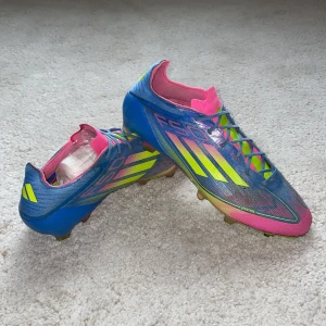 ADIDAS F50 ELITE FG CELESTIAL VICTORY - BLÅ/LUCID LEMON/LUCID PINK - Säljer ett par ADIDAS F50 ELITE FG CELESTIAL VICTORY - BLÅ/LUCID LEMON/LUCID PINK fotbollsskor. Skorna har snörning, platt sula med dobbar och är tillverkade i syntetmaterial. De har en sportig design med tydliga F50-loggor och klassiska Adidas-ränder på sidorna. Ingen påse ingår.  Skicka vid frågor eller funderingar.         Mvh Axel 🤝 