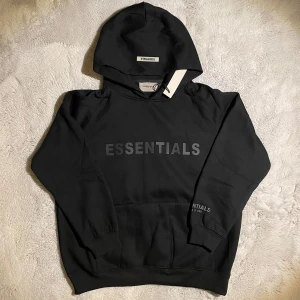 Hoodie Essentials Fear of God - Svarta Essentials Fear of God hoodie är i utmärkt skick med taggar kvar.  ⭐️ Skick: Oanvänd / Ny 🎲 Storlek: M 🎨 Färg: Svart 📦 Snabb och noggrann frakt.