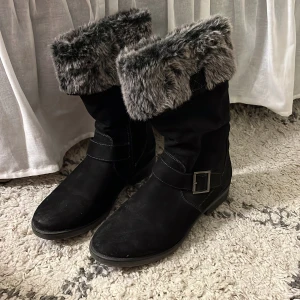 Svarta boots med fuskpäls och spänne - Snygga svarta boots med mjuk grå fuskpäls upptill och dekorativt spänne i metall. Endast använda två gånger. Skorna har grov sula för bra grepp och dragkedja på sidan för enkel påtagning. Perfekta för kalla dagar och ger en cool vinterlook 🖤