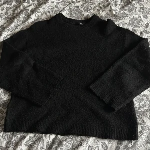 Svart stickad tröja  - En svart stickad tröja med rund hals och långa ärmar. Tröjan har en enkel och stilren design med ribbade muddar vid ärmslut och nederkant. Perfekt för lager-på-lager och passar till allt.