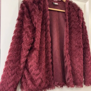 Vinröd pälsjacka från hm - Mysig vinröd pälsjacka från hm med lång luddig fuskpäls och öppen front. Jackan har lång ärm och en loose fit som ger en chill vibe. Perfekt för dig som vill sticka ut med en trendig look i höst och vinter.