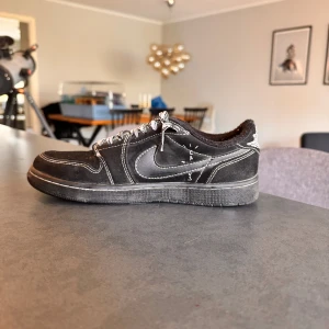 Svarta Nike sneakers - Svarta Nike sneakers med kontrasterande vita sömmar och snörning. Skon har en klassisk låg siluett och är tillverkad i mocka och syntetmaterial. Swoosh-loggan syns tydligt på sidan och det finns unika vita detaljer på hälen och sidan.
