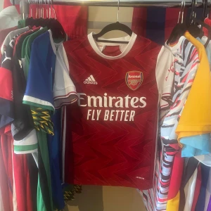 Arsenal hemmatröja Adidas 13-14 år, äkta - Säljer en Arsenal hemmatröja från Adidas i röd och vit med blixtmönster. Tröjan är i bra skick och i storlek 164 (13/14år), äkta