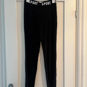 Svarta tights med sportig midja - Svarta tights med elastisk midja där det står SPORT i vitt. Tillverkade i mjuk bomull med lite spandex för stretchig passform. 