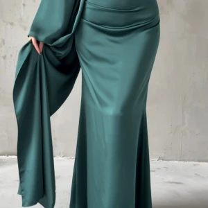 Grön långklänning med drapering - Säljer en elegant grön långklänning i glansigt material med långa vida ärmar och snygg drapering i midjan. Klänningen har en figurnära passform upptill och faller snyggt längs kroppen. Perfekt för dig som vill sticka ut med en unik och stilren look.tagen är fortfarande på den! 