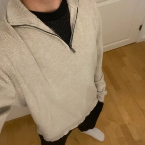 Beige stickad half zip-tröja - Säljer en beige stickad tröja med half zip-dragkedja och hög krage. Tröjan har en relaxed passform och är långärmad, perfekt för lager-på-lager. Enkel och stilren design som funkar till det mesta.