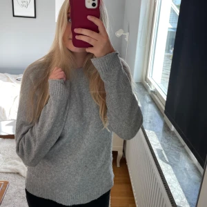 Grå stickad tröja från Vero Moda - Mysig grå stickad tröja från Vero Moda i storlek S. Tröjan har en klassisk rund halsringning, långa ärmar och ribbade muddar vid ärmslut och nederkant. Perfekt för lager-på-lager och chill dagar.