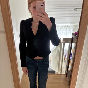 Svart kavaj från Soaked in Luxury - Snygg svart kavaj med markerade axlar och coola veckade detaljer på ärmarna. Kavajen är figursydd, har två knappar framtill och en djup v-ringning. 