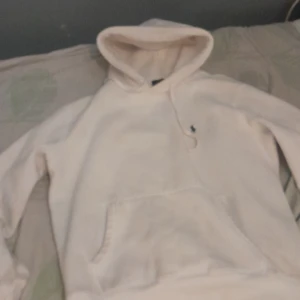 Vit hoodie från Polo Ralph Lauren - Vit hoodie från Polo Ralph Lauren med klassisk broderad logga på bröstet. Tröjan har huva med snörning och en stor magficka framtill. Mjuk och skön, perfekt för chill dagar. Snygg och enkel design som funkar till det mesta.