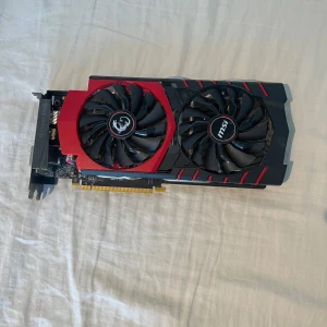 MSI Gaming Graphics Card gtx 970 - MSI gaming grafikkort med dubbla fläktar för effektiv kylning. Snygg röd och svart design, PCIe-anslutning. Kortet ser ut att vara i gott skick utan synliga skador eller större slitage. Perfekt för gaming eller uppgradering av din stationära dator.