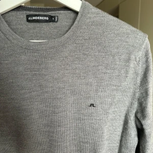 Grå stickad tröja från J.Lindeberg - Snygg grå stickad tröja från J.Lindeberg med rund halsringning och diskret logga på bröstet. Tröjan har långa ärmar och ribbade muddar vid ärmslut och nederkant. Nypris 1500kr säljer för 499kr 