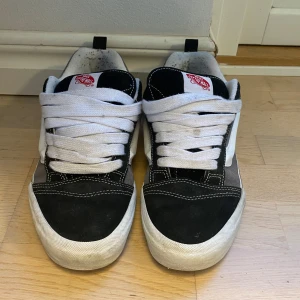 Vans Knu Skool Svart/Grå - Vans Knu Skool sneakers i svart och grå mocka med vit sula och vit sidostrip. Skorna har en fet vit snörning och rund tå. Perfekta för en streetwear-look och passar till det mesta.