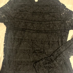 Svart spetsblus med lång ärm - Säljer en svart blus i genombruten spets med lång ärm. Toppen har ett feminint och elegant uttryck med fina spetsdetaljer över hela plagget. Perfekt för dig som gillar en stilren men ändå romantisk look.
