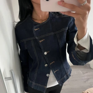 Mörkblå jeansjacka med asymmetrisk knäppning gina tricot - Säljer en snygg mörkblå jeansjacka med cool asymmetrisk knäppning och silvriga knappar. Kan användas som både topp och jacka. Perfekt för dig som vill ha en unik twist på den klassiska denimlooken. 