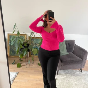 Ribbad rosa långärmad topp - Säljer en ribbad långärmad topp i stark rosa färg. Toppen har en snygg v-ringad urringning och lätt utsvängda ärmslut. Modellen är figurnära och croppad, perfekt att styla med höga byxor. Materialet är mjukt och stretchigt.