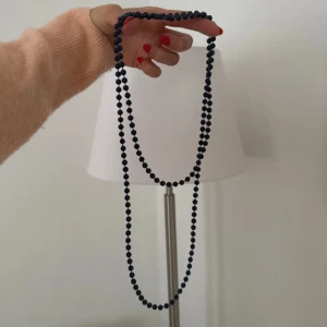 Långt svart/blått pärlhalsband - Snyggt långt halsband med svarta pärlor. Perfekt att bära i flera lager för en cool och stilren look. Halsbandet har små, runda pärlor som ger en klassisk känsla och passar till många olika outfits.