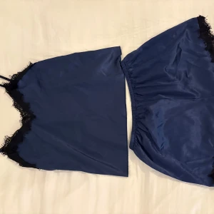 Mörkblå pyjamaset med spetsdetaljer - Säljer en mörkblå linnetopp med tunna axelband och svarta spetsdetaljer längs urringningen. Helt oanvänd.